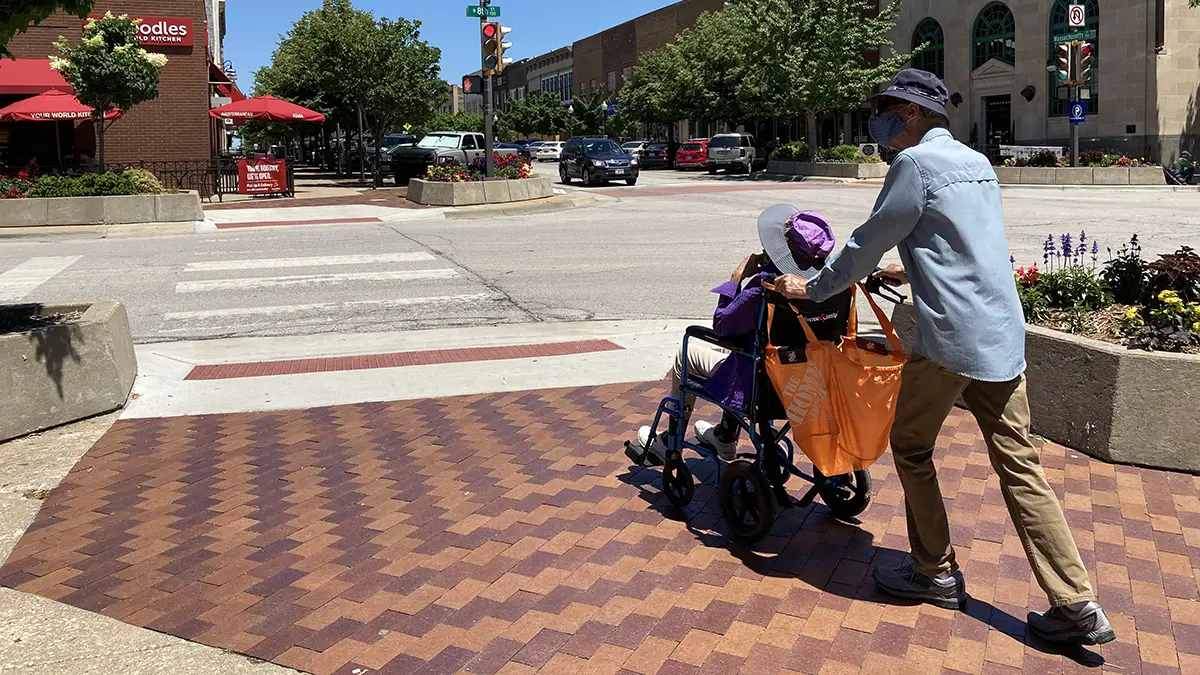 Peron pushing another person in a wheelchair over a brick sidewalk in Downtown Lawrence